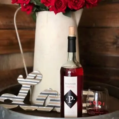 bottle of rosé wine next to a glass of rosé, red roses and a metal sign that says "love"